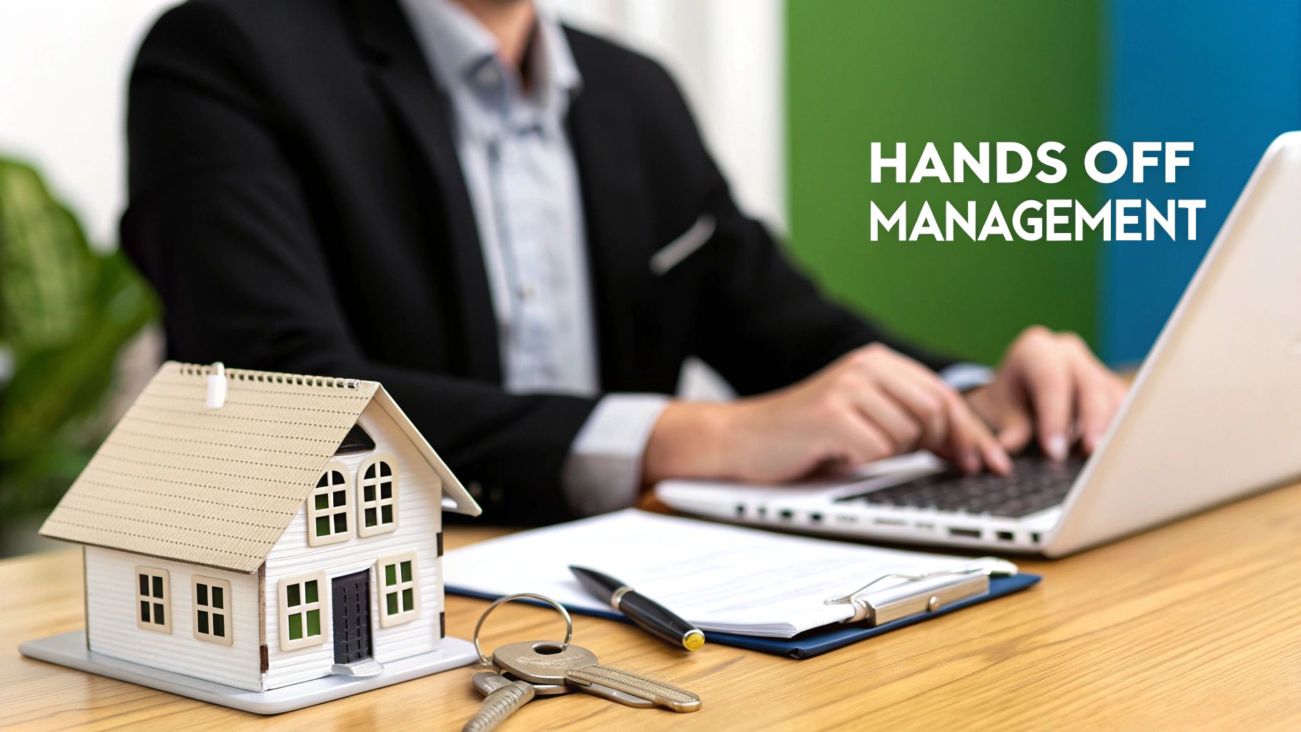 A person uses a laptop on a desk with a model house and keys, offering hands-off property management.