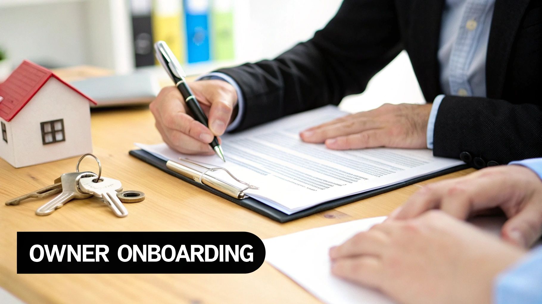 A person signs owner onboarding documents with keys and a model house on the table.