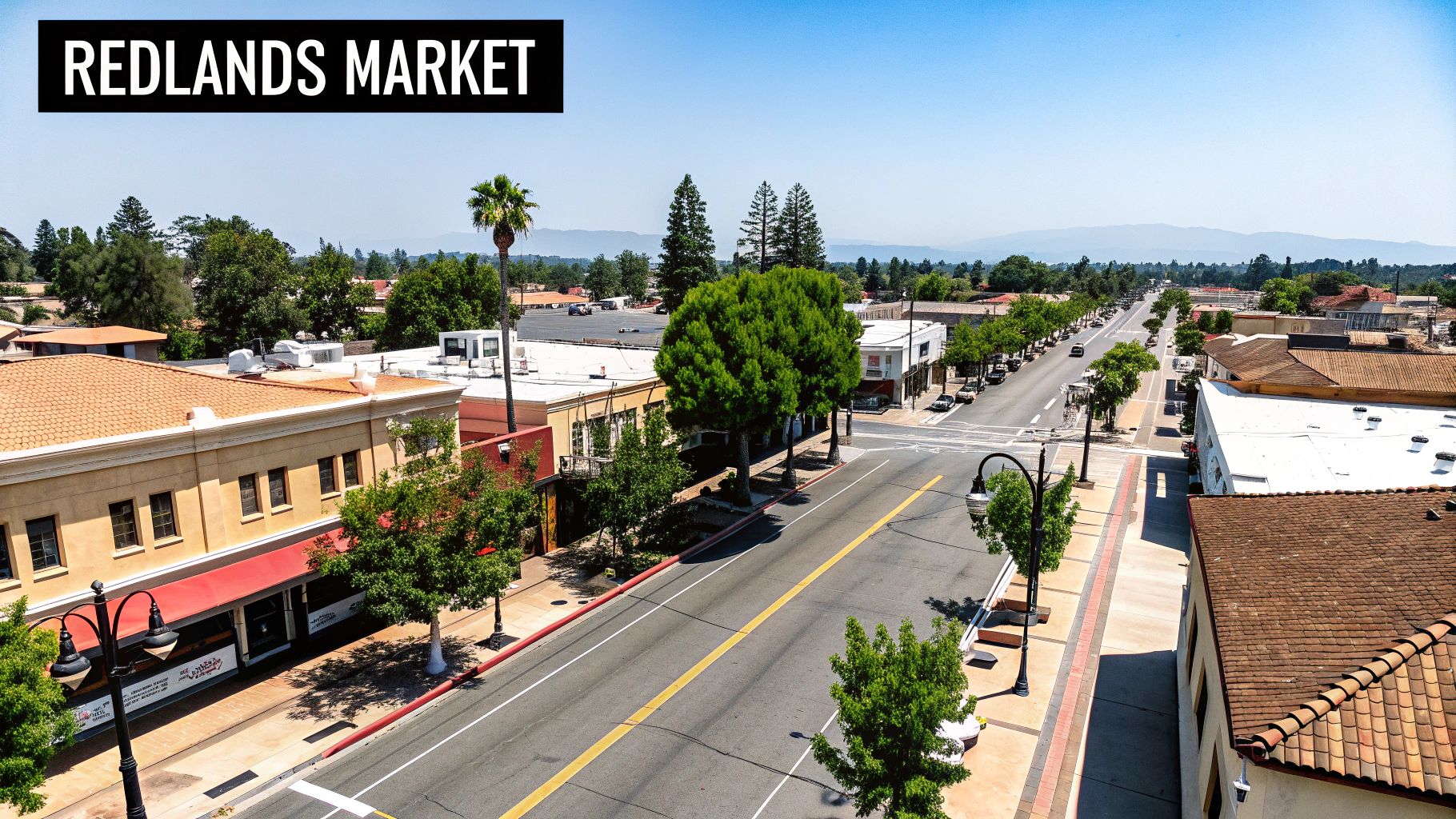 Aerial view of a sunny downtown street in Redlands with commercial buildings, trees, and cars.